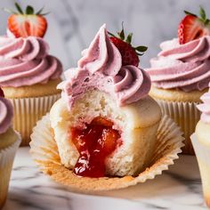 cupcakes with pink frosting and strawberries in the middle on a marble surface