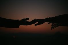 two hands reaching out towards each other at sunset