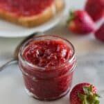 a jar of strawberry jam next to sliced strawberries