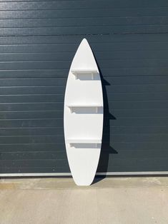 a white surfboard leaning against a garage door with shelves on the wall above it