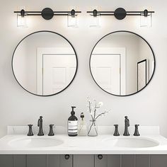 two round mirrors on the wall above double sinks in a white bathroom with black faucets