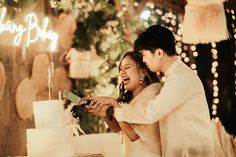 a newly married couple cutting their wedding cake at the end of the night with lights in the background