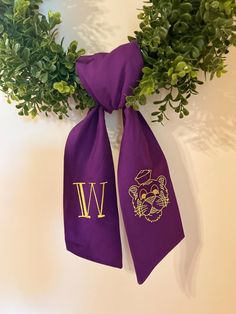 two purple scarfs with the letter w on them hanging from a wall next to green plants