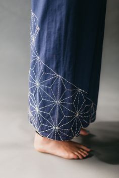 a person standing with their feet on the ground wearing blue pants and sandals, while they both have beaded designs on them