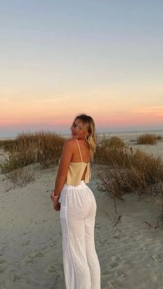 a woman standing on top of a sandy beach next to tall grass and sand dunes