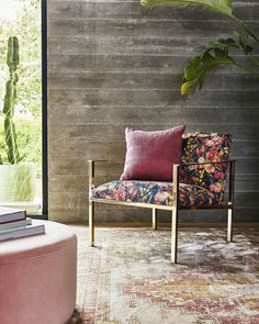 a pink chair sitting in front of a wooden wall next to a potted plant