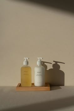 two soap dispensers sitting on top of a wooden tray next to each other