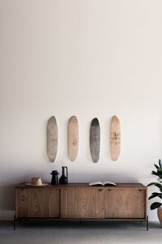 three skateboards are mounted on the wall above a wooden cabinet and potted plant