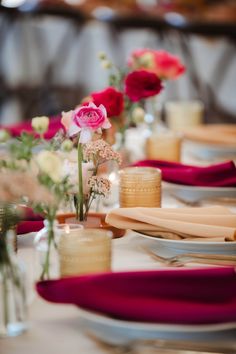 the table is set with pink and white flowers in vases, candles and napkins