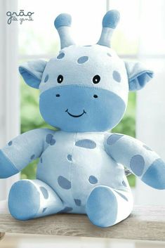 a blue stuffed giraffe sitting on top of a wooden table next to a window