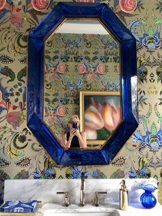 a person taking a selfie in front of a mirror with flowers on the wall