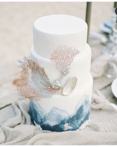 a white and blue wedding cake sitting on top of a wooden table next to candles