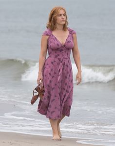 a woman in a purple dress is walking on the beach with her purse and handbag