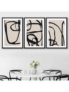 three black and white paintings hanging on the wall above a dining room table with four chairs