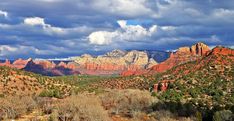 the mountains are covered in red rocks and green trees, under a cloudy blue sky