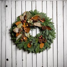 a green wreath with pine cones and other decorations on a white wooden background, hanging from the side of a wall