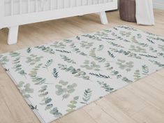 a white rug with green leaves on it in front of a crib and baby's bed