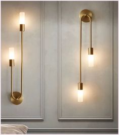 two gold wall lights on the side of a white wall next to a bed in a room