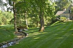 there is a small wooden bridge in the middle of this grassy area that leads to a large house