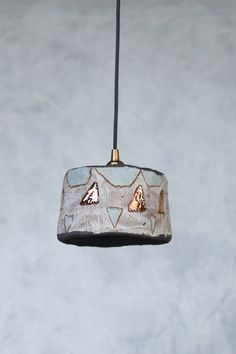 a wooden light fixture hanging from a black cord with white and brown designs on it