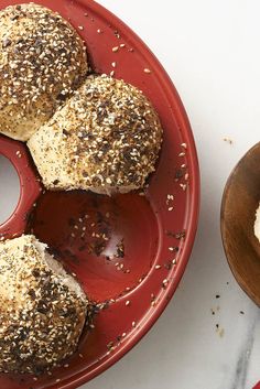 a red plate topped with three bagels on top of a white counter next to a wooden bowl