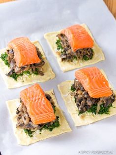 four square pieces of bread with salmon on top and mushrooms in the middle, sitting on a sheet of parchment paper