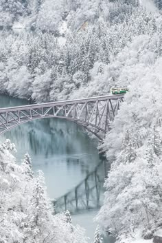 a train crossing a bridge over a river surrounded by snow covered trees and evergreens