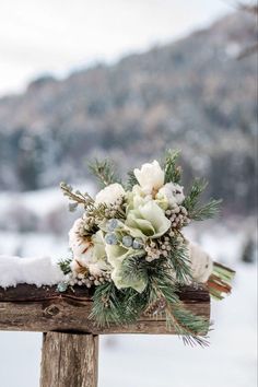 a bouquet of white flowers sitting on top of a wooden post in front of snow covered mountains