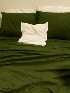 an unmade bed with green sheets and pillows