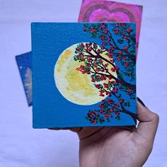 a hand holding up a small card with a tree on it and the moon in the background