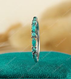 a ring with turquoise stones is sitting on a green cloth in front of a white background