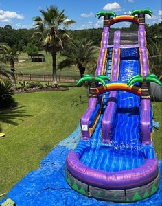 an inflatable water slide with palm trees and blue tarp on the ground