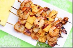 grilled shrimp and pineapple skewers on a white plate with a wedge of pineapple