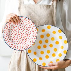 a woman holding two plates with orange polka dots on them, one is white and the other is yellow