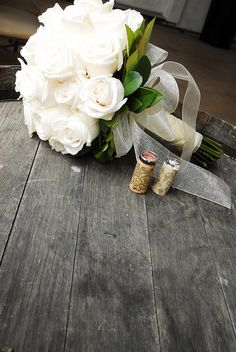 a bouquet of white roses sitting on top of a wooden table next to two wine corks