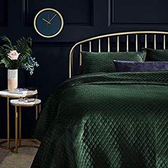 a bed with green bedspread and pillows in front of a black wall next to a side table