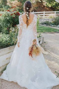 a woman in a white wedding dress is holding a bouquet and looking down at the ground