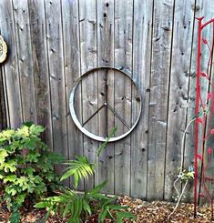 a metal peace sign sitting on the side of a wooden fence next to a plant