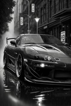 a black and white photo of a sports car in the rain on a city street