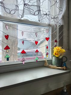 a vase with yellow flowers sitting on a window sill next to a string of red and green umbrellas