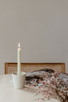 a lit candle sitting on top of a white table next to a book and flowers