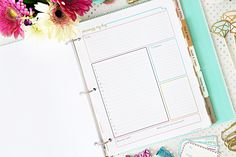 a binder, notepad and flowers on a desk with paper clippings