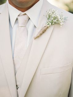 a man in a white suit and tie with a boutonniere on his lapel