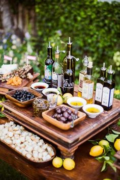 an assortment of food and wine on a table outdoors with lemons, grapes, nuts, and other foods