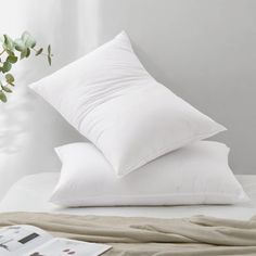 two pillows on top of a bed next to a plant