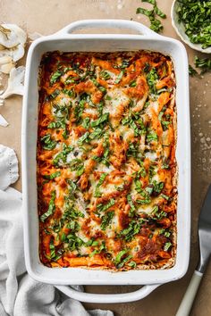 a white casserole dish filled with lasagna sauce and fresh basil leaves