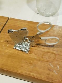 a pair of scissors on a cutting board with some tin foil next to the blades