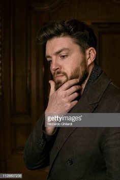 a man with a beard is looking down at his hand on his chin while standing in front of a wooden door