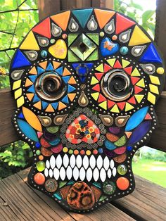 a colorful skull made out of glass sitting on top of a wooden table next to trees