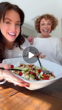 two women are smiling and one is holding a plate with vegetables on it while the other woman smiles